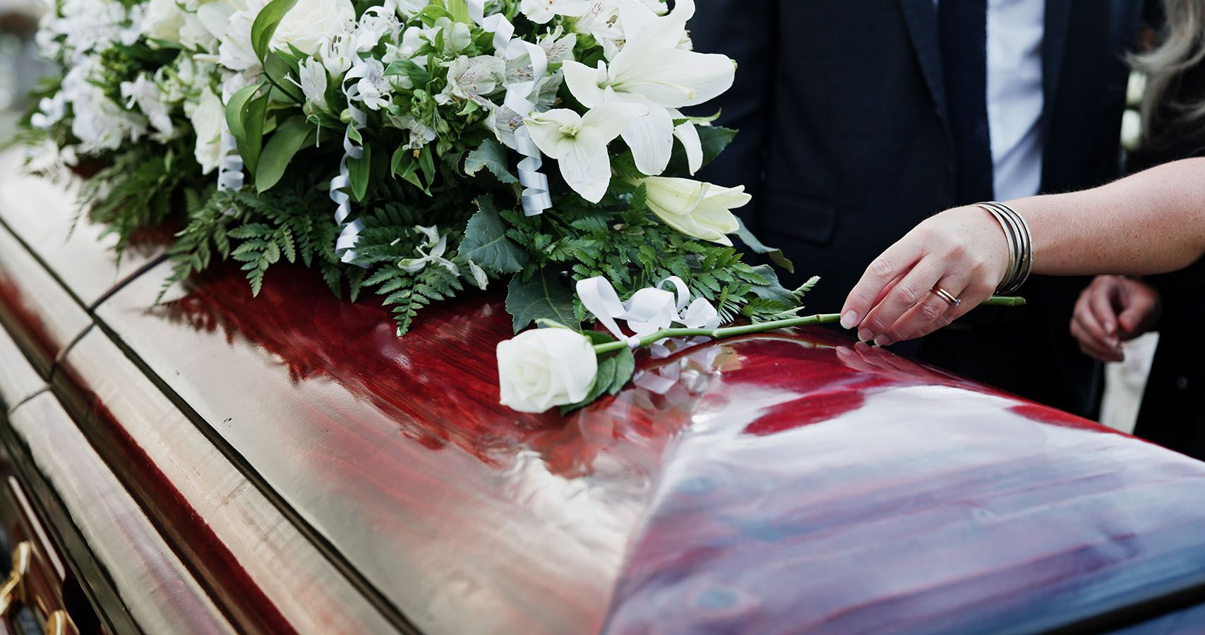 White flowers on a coffin with a hand placing a rose at a funeral