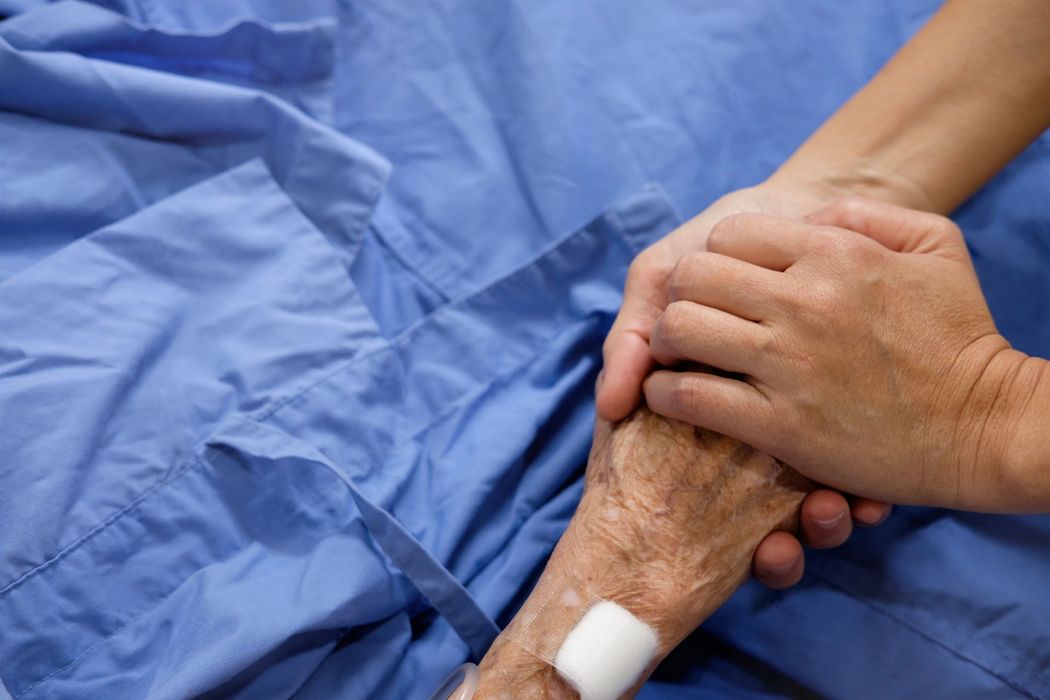 Due mani strette attorno al braccio di un paziente con un braccialetto ospedaliero, su lenzuola blu.