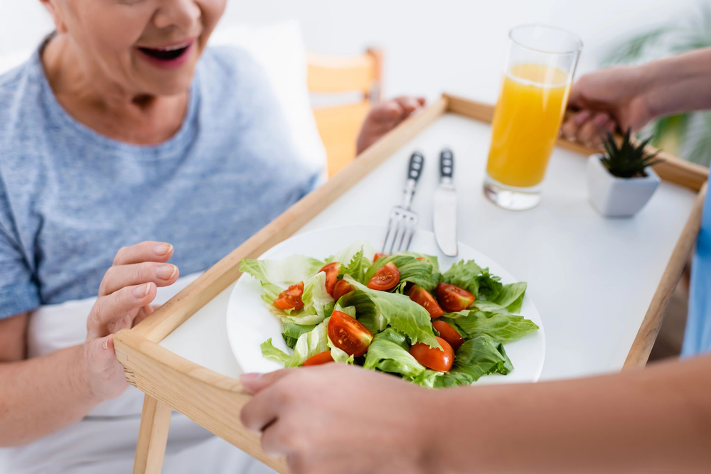 Una persona serve un vassoio con insalata e succo d'arancia a un tavolo luminoso.