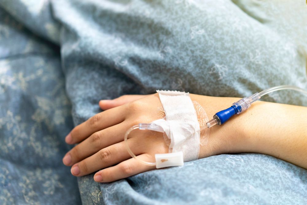 Linea endovenosa fissata con del nastro adesivo a una mano appoggiata su una coperta blu.