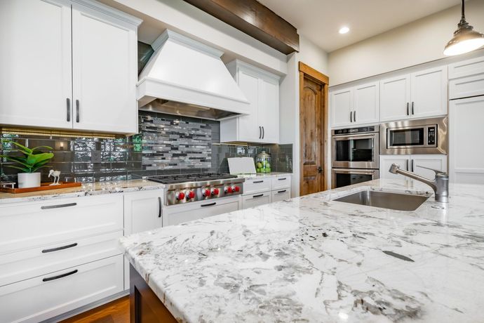 A kitchen with white cabinets , granite counter tops , stainless steel appliances and a large island.