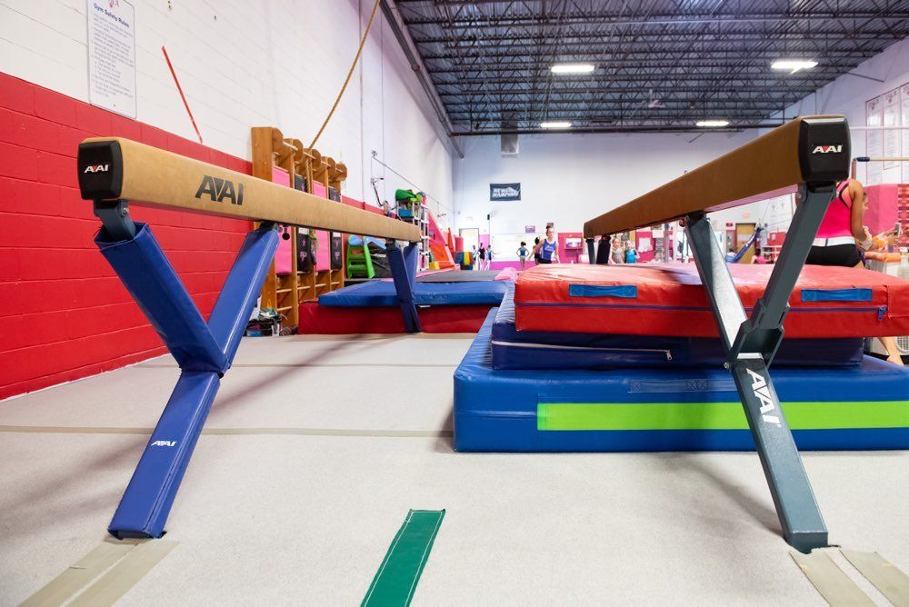Two balance beams in a gym, with blue and gray supports, on a blue mat.