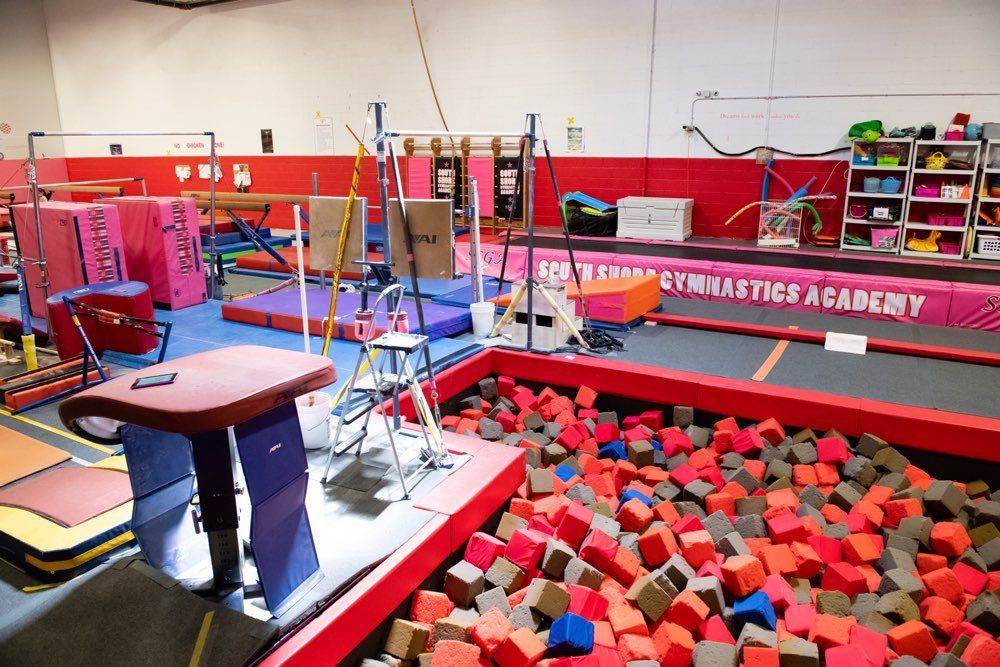 Gymnastics gym with various equipment, including a foam pit, vault, bars, and balance beams.
