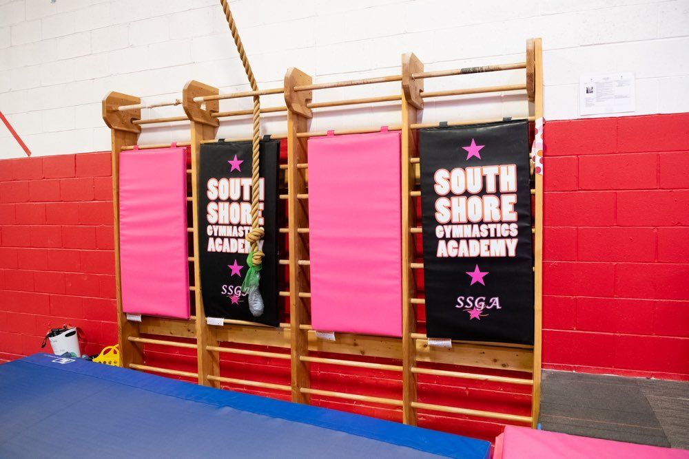 Gymnasium wall with padded mats and a climbing rope; 
