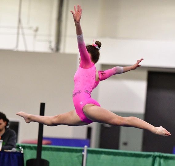 Gymnast in a pink leotard performs a split leap in mid-air.