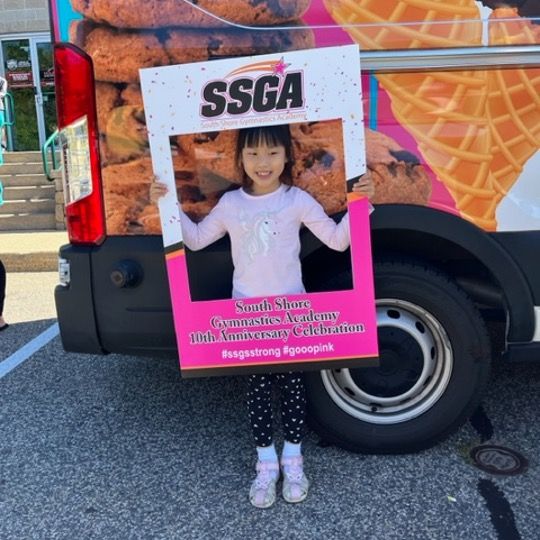 Girl posing with a photo frame in front of an ice cream truck; frame says 