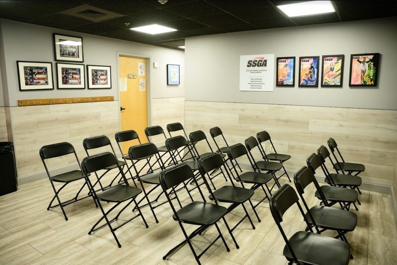 A small room with rows of black folding chairs facing a wall with framed art and a closed yellow door.