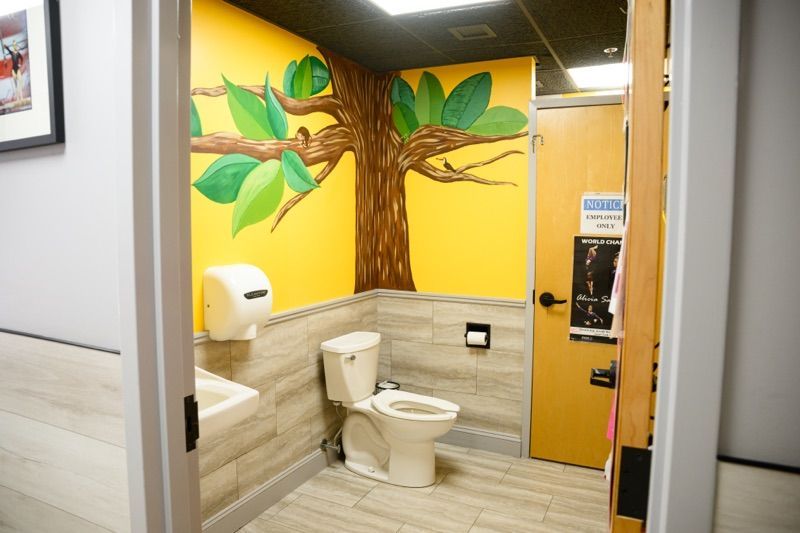 Bathroom with tree mural on yellow wall, toilet, and sink. Wooden door.