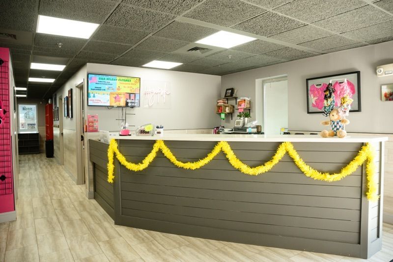 Reception area with gray desk, yellow garland, and hallway to treatment rooms.