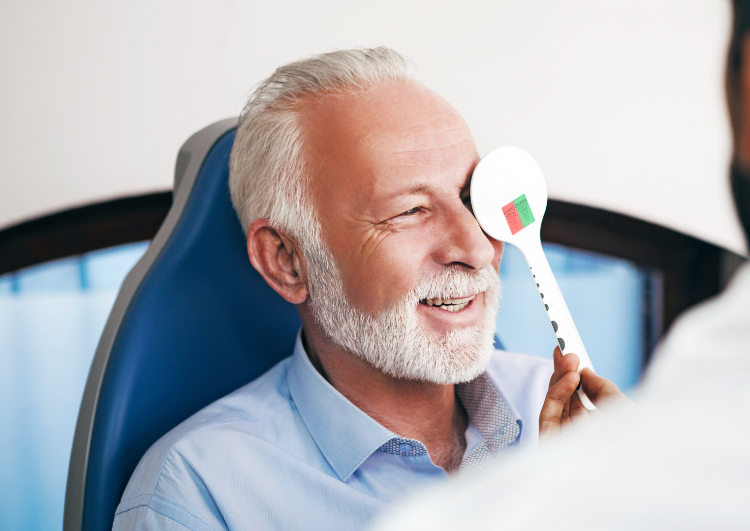 Smiling man in a blue shirt undergoing a dental exam with a mirror in a clinic