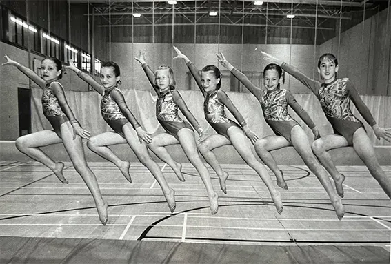 A group of young girls are jumping in the air in a gym.