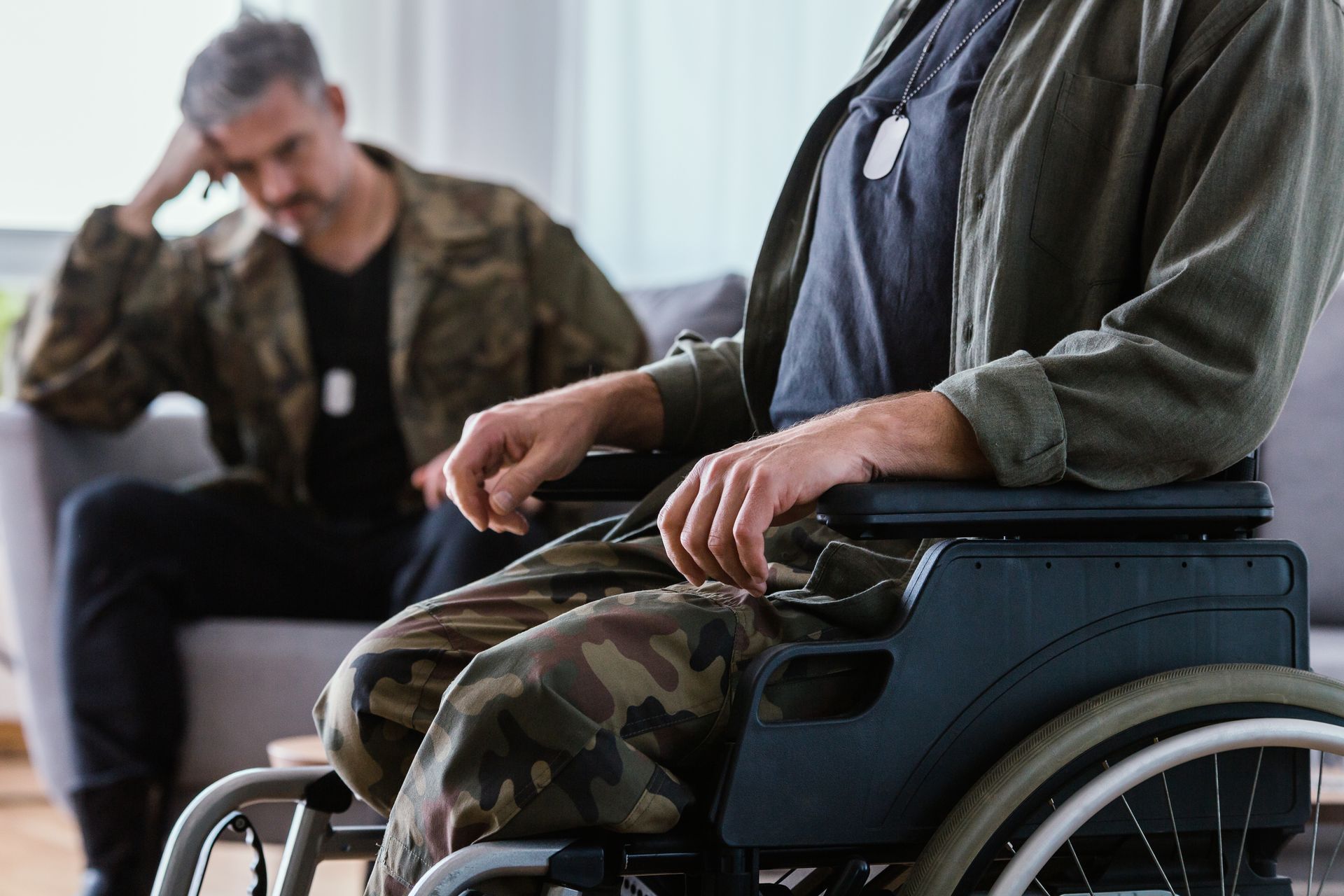 A man in a wheelchair is talking to another man on a couch.