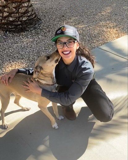 A woman wearing glasses and a hat is hugging a dog