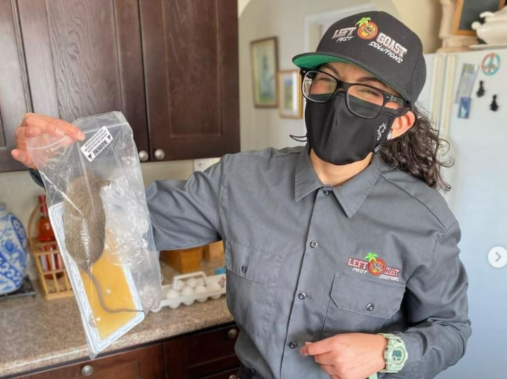 A woman wearing a mask and a hat is holding a plastic bag.