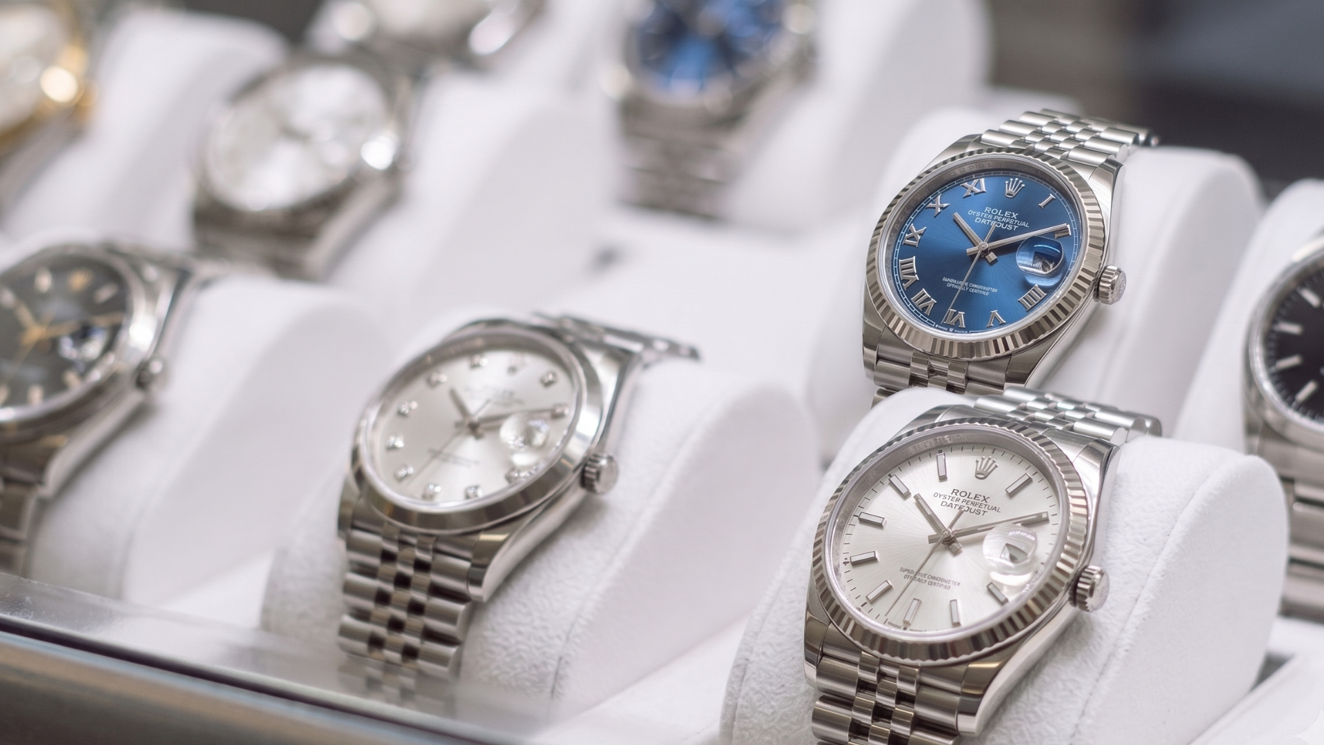Display of luxury wristwatches on white stands, including silver and blue-faced watches.