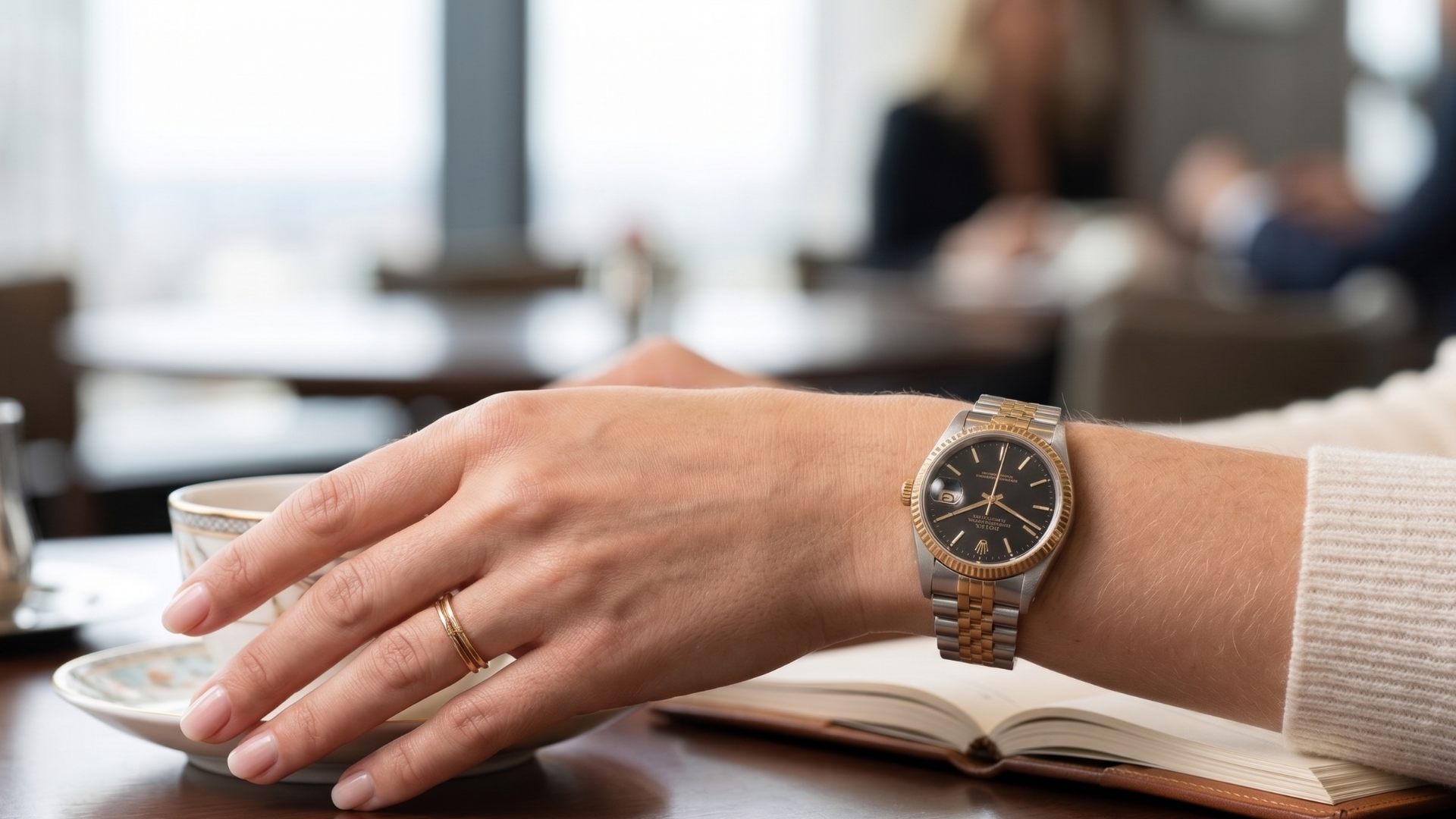 Hand with wristwatch resting on an open book at a café table