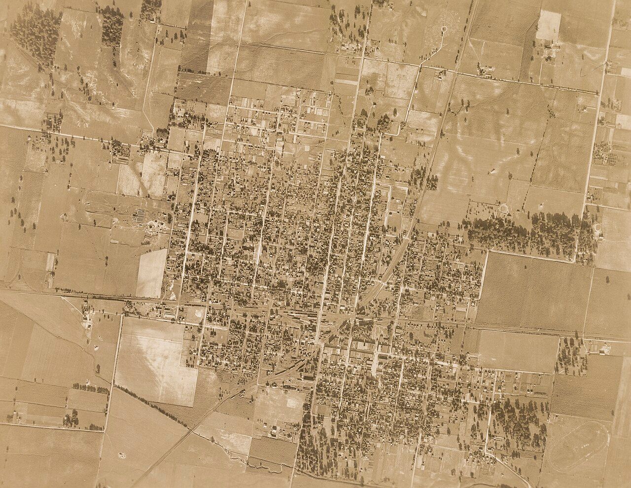 Aerial view of a rural town with a grid-like layout, surrounded by fields and scattered trees.