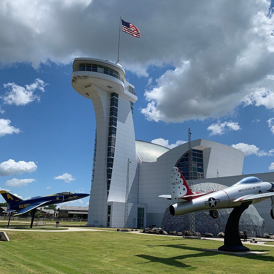 White museum with control tower and jets, American flag waving under blue sky.