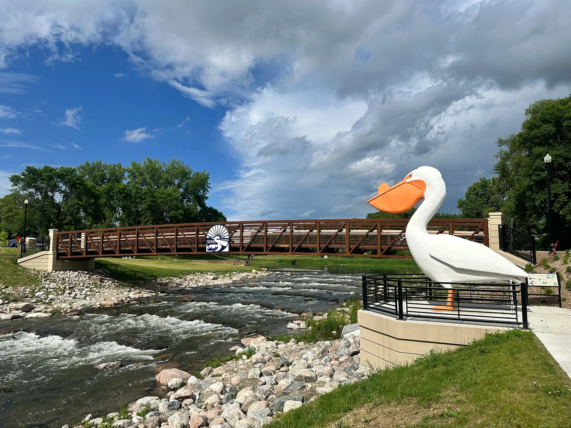 A large white pelican statue is standing next to a river.