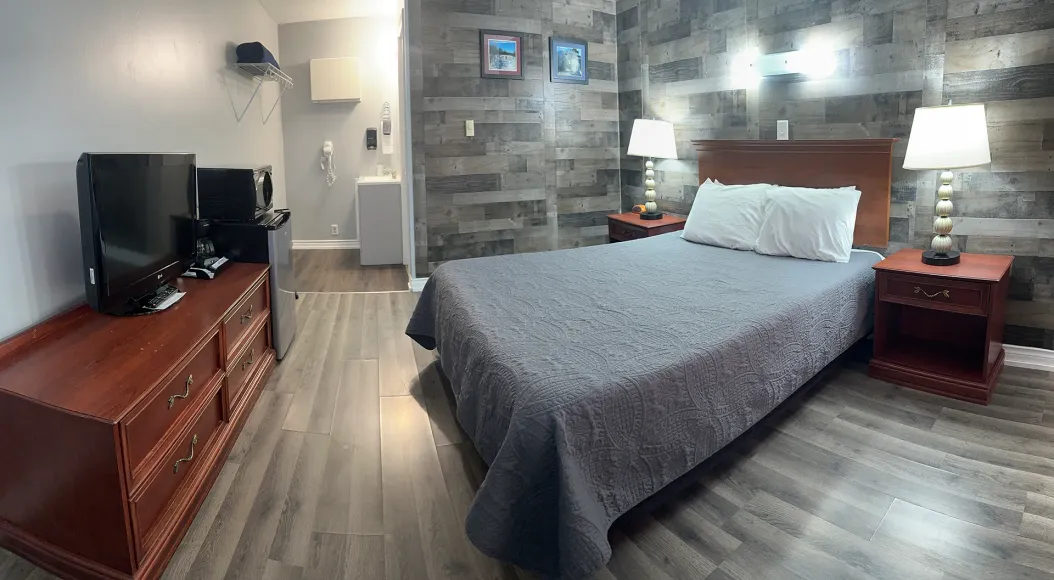 A hotel room with a bed , dresser , television and nightstand.