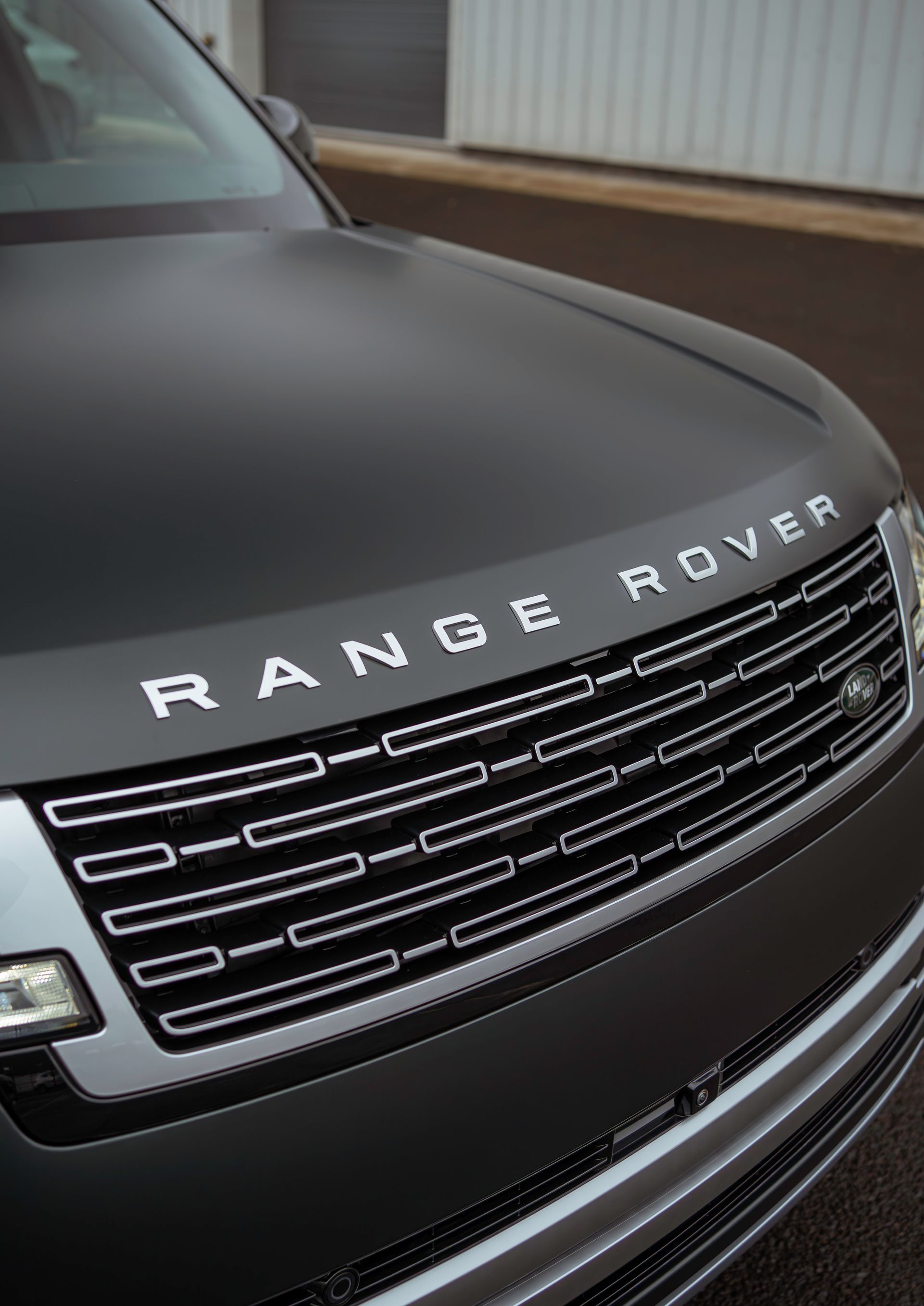 Close-up of a black Range Rover front grille with silver lettering and headlights on display