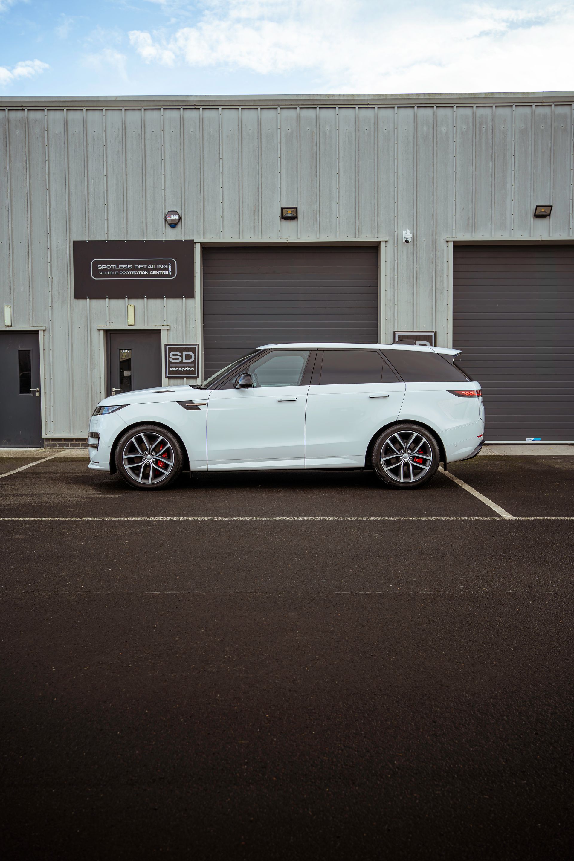 White SUV parked outside a gray industrial building with garage doors and a sign.