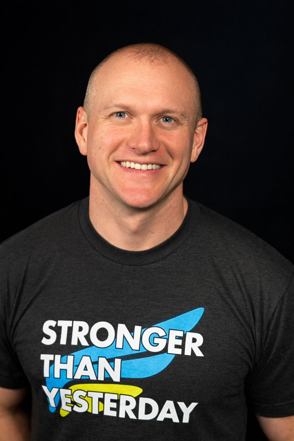 Smiling person in a black T-shirt with the text “Stronger Than Yesterday” on a dark background