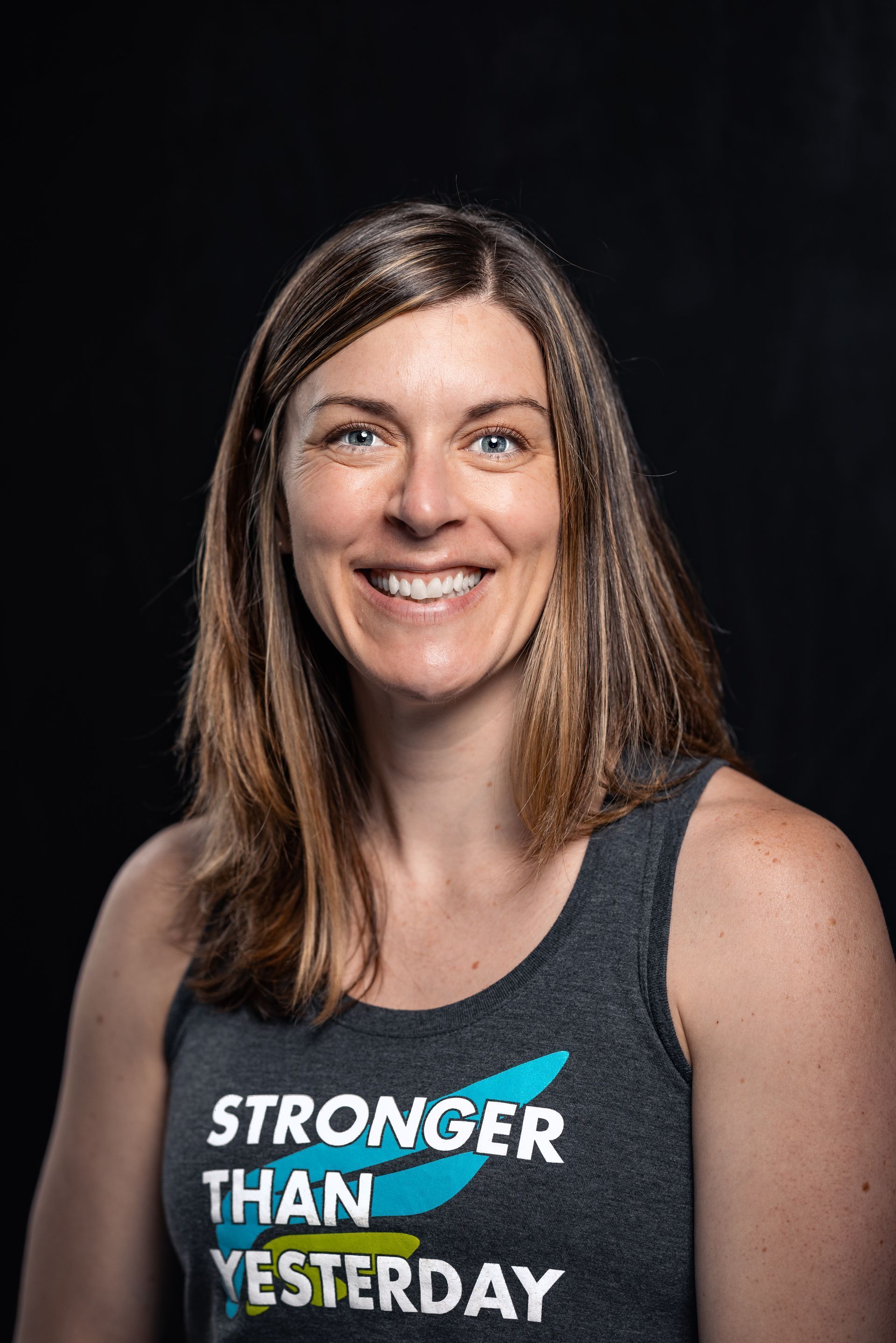 Smiling person in a dark tank top with the words “Stronger Than Yesterday” on a black background