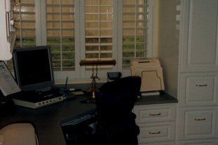 A desk with a computer and a chair in front of a window.