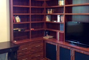 A room with a desk , shelves , drawers and a flat screen tv.