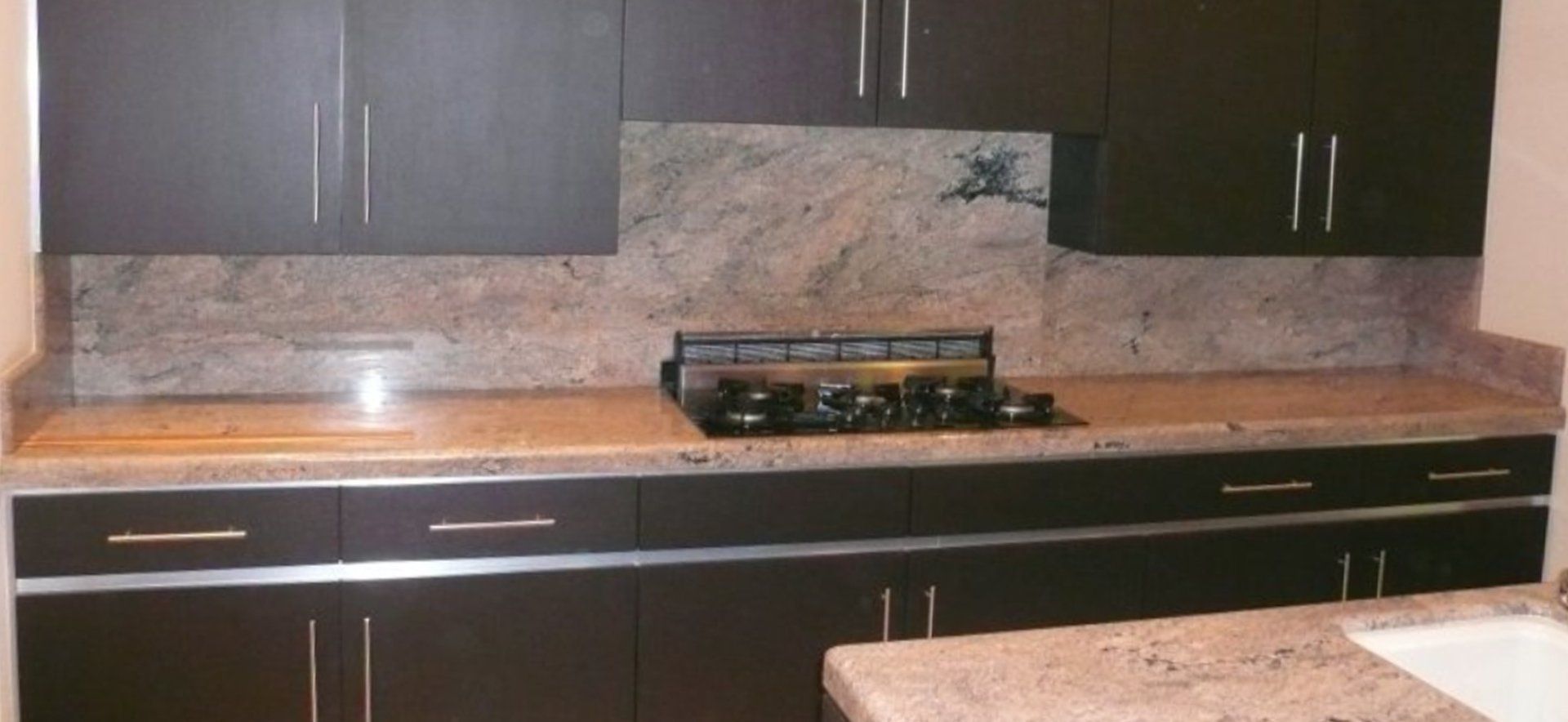 A kitchen with black cabinets , granite counter tops , and a stove top oven.