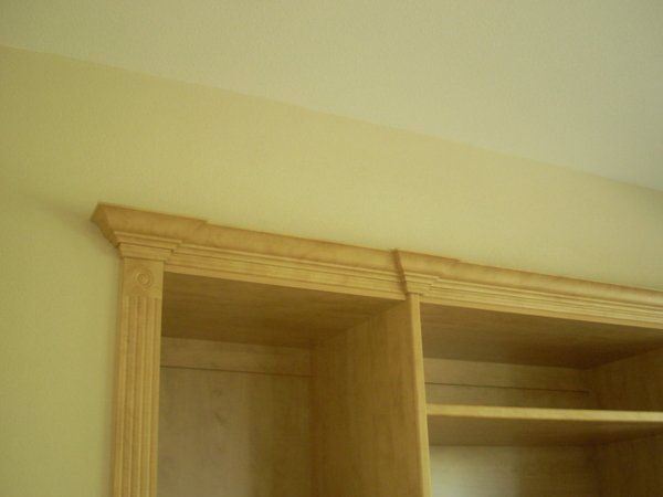 A close up of a wooden bookshelf with a ceiling in the background.