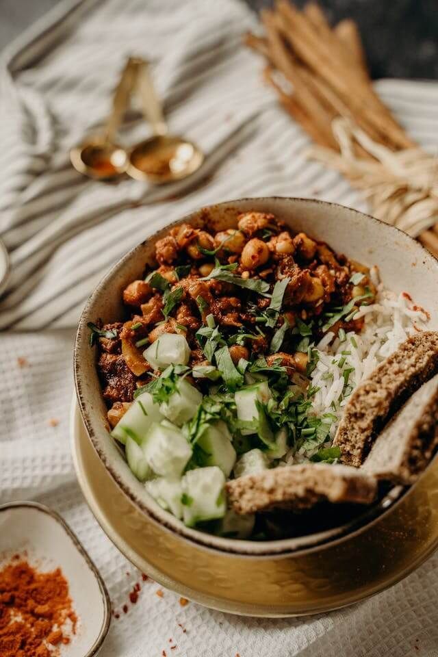 Bowl of chickpeas and rice, garnished with cucumber and parsley, served with bread.