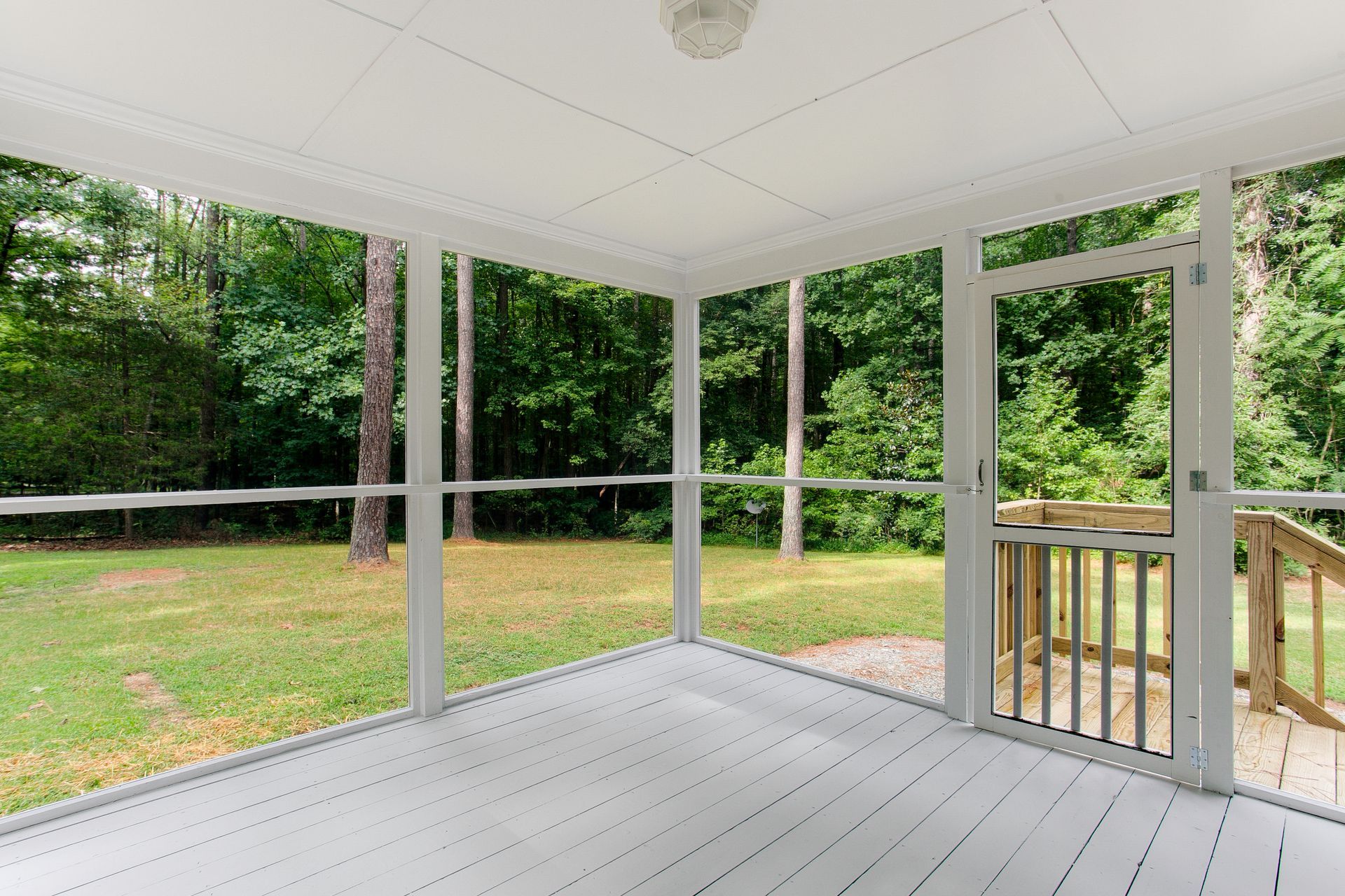 A screened in porch with a wooden deck and trees in the background.