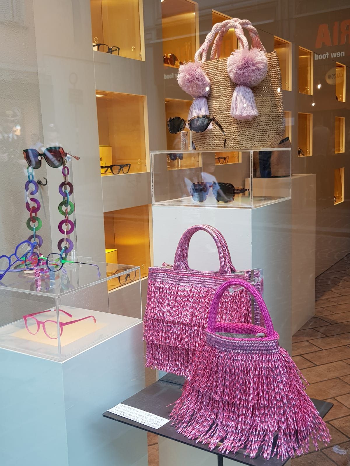 Borsette rosa con frange e un accessorio con pompon soffice esposti nella vetrina di una boutique.