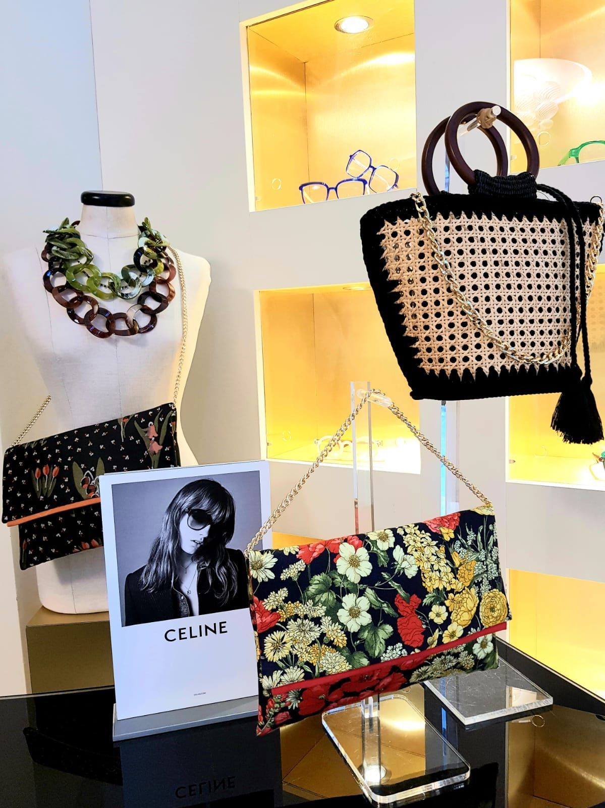 Esposizione di moda con borse, collane e rivista Celine su scaffali illuminati.