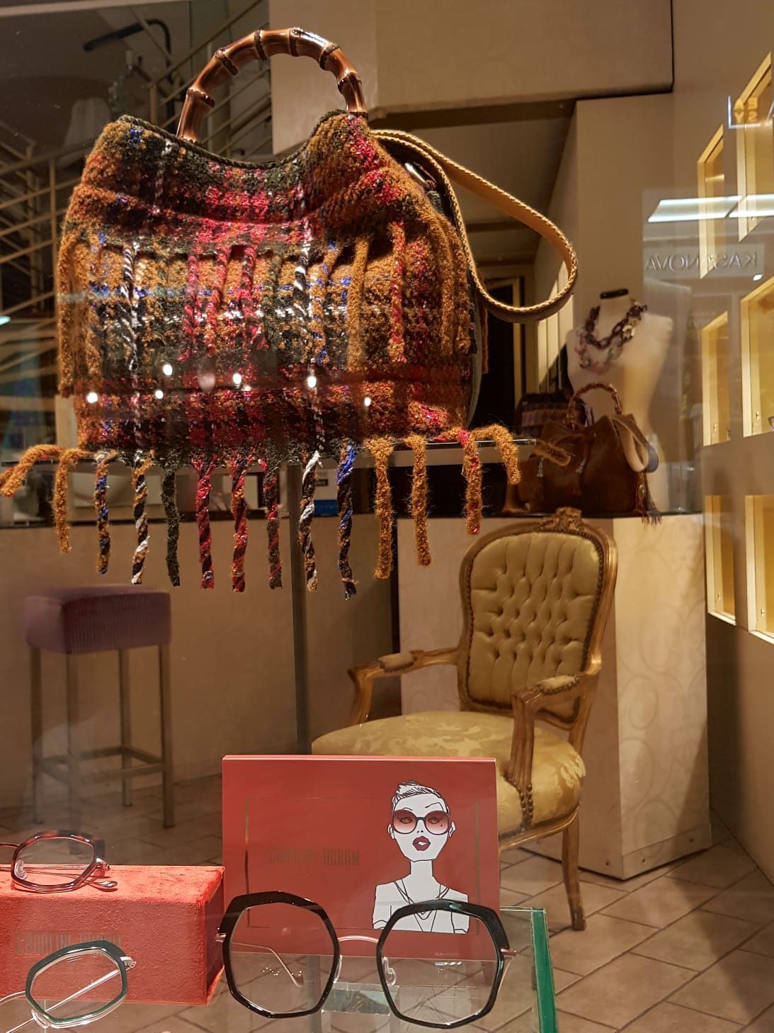 In una vetrina, una colorata borsa intrecciata è esposta insieme a occhiali, una sedia e un piccolo poster.