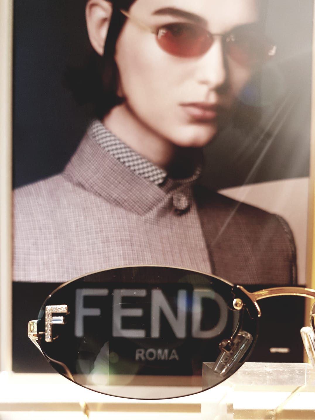 Occhiali da sole Fendi esposti davanti a un poster di moda.