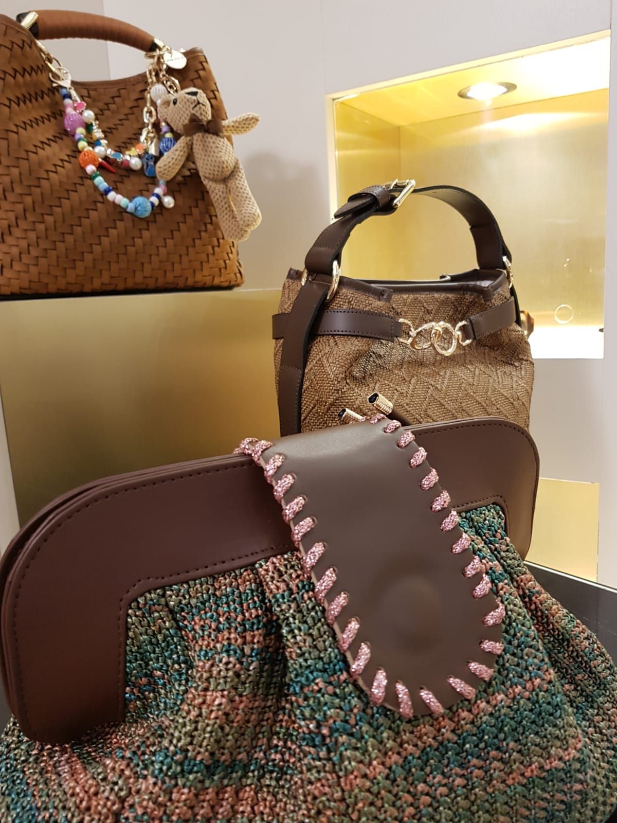 In un ambiente da boutique sono esposte diverse borse assortite, tra cui una tote bag intrecciata marrone e borsette a fantasia.