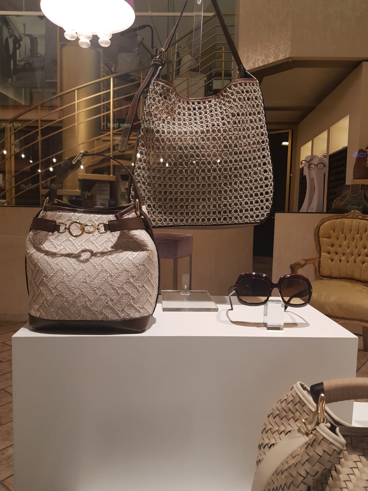 Borse e occhiali da sole esposti su un piedistallo bianco all'interno di una boutique.