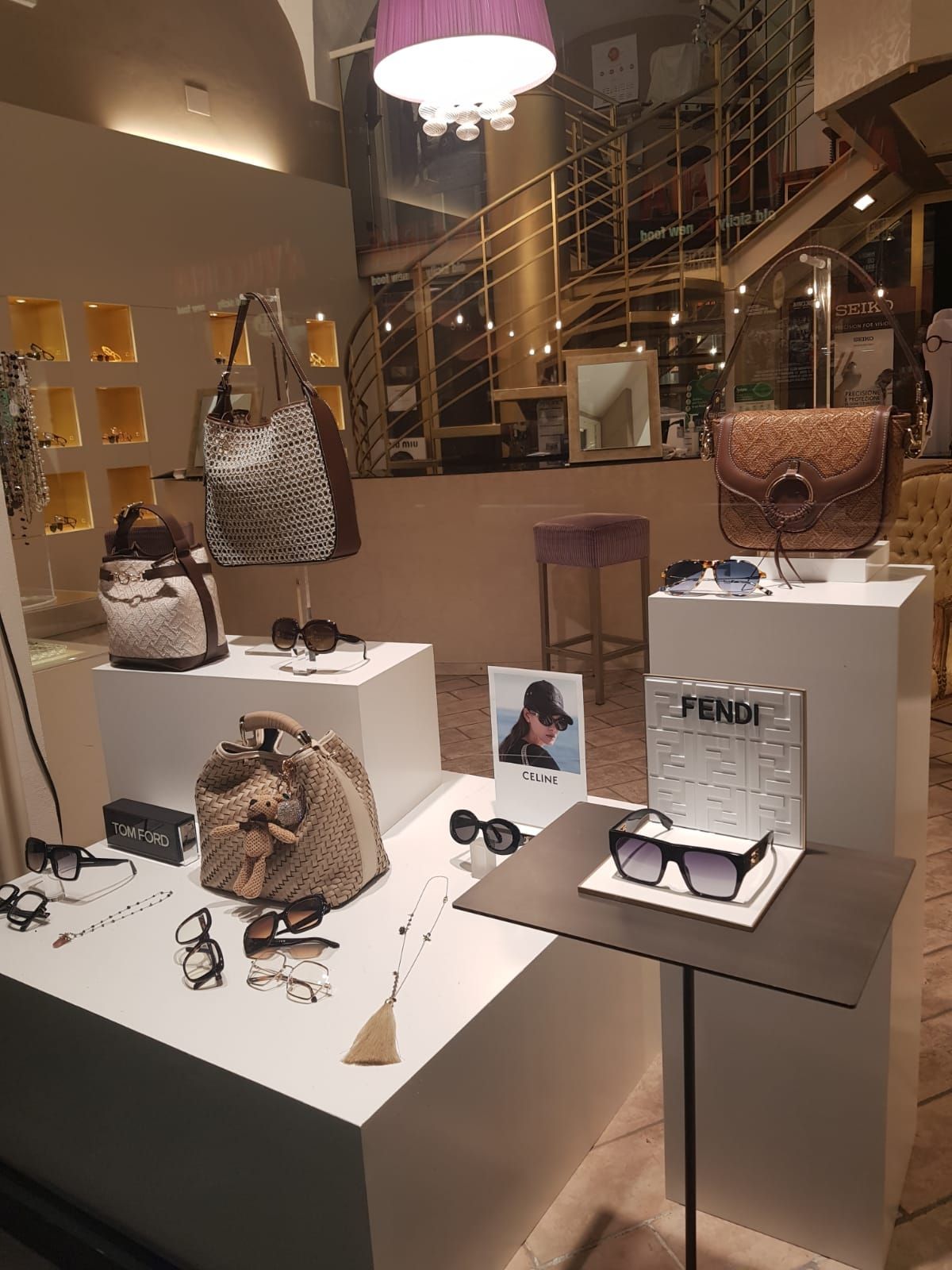 Borse e accessori di lusso esposti su piedistalli bianchi nella vetrina di una boutique.