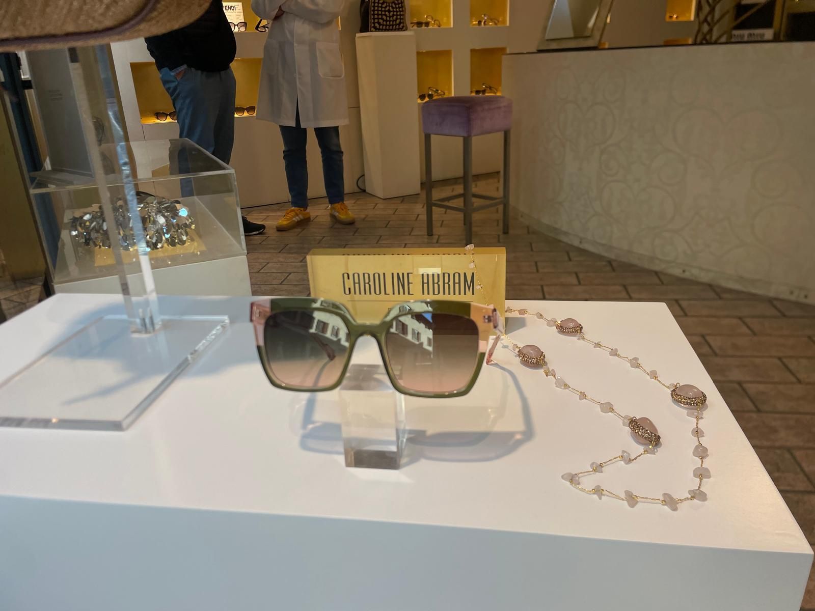 Occhiali da sole e una collana di gioielli esposti su un tavolo bianco nella vetrina di un negozio.