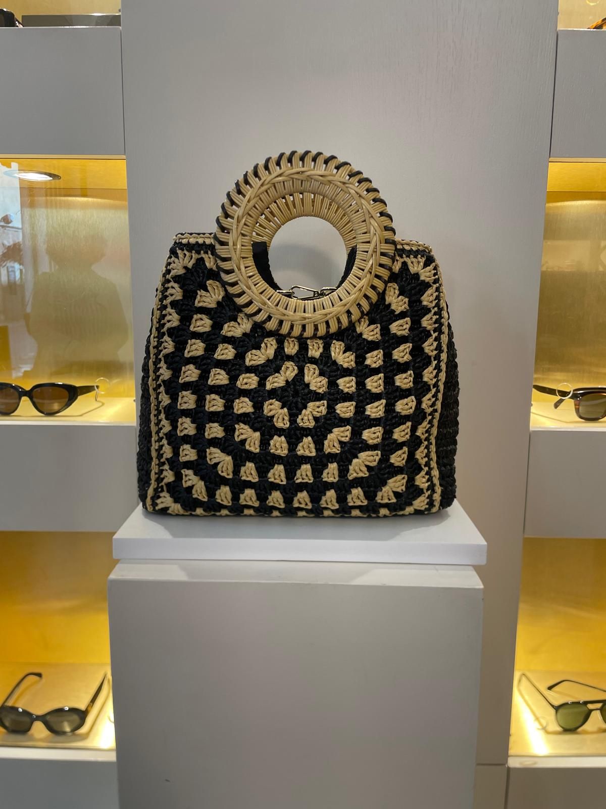 Borsa a mano intrecciata nera e oro con manico circolare, esposta su un piedistallo nella vetrina di una boutique.