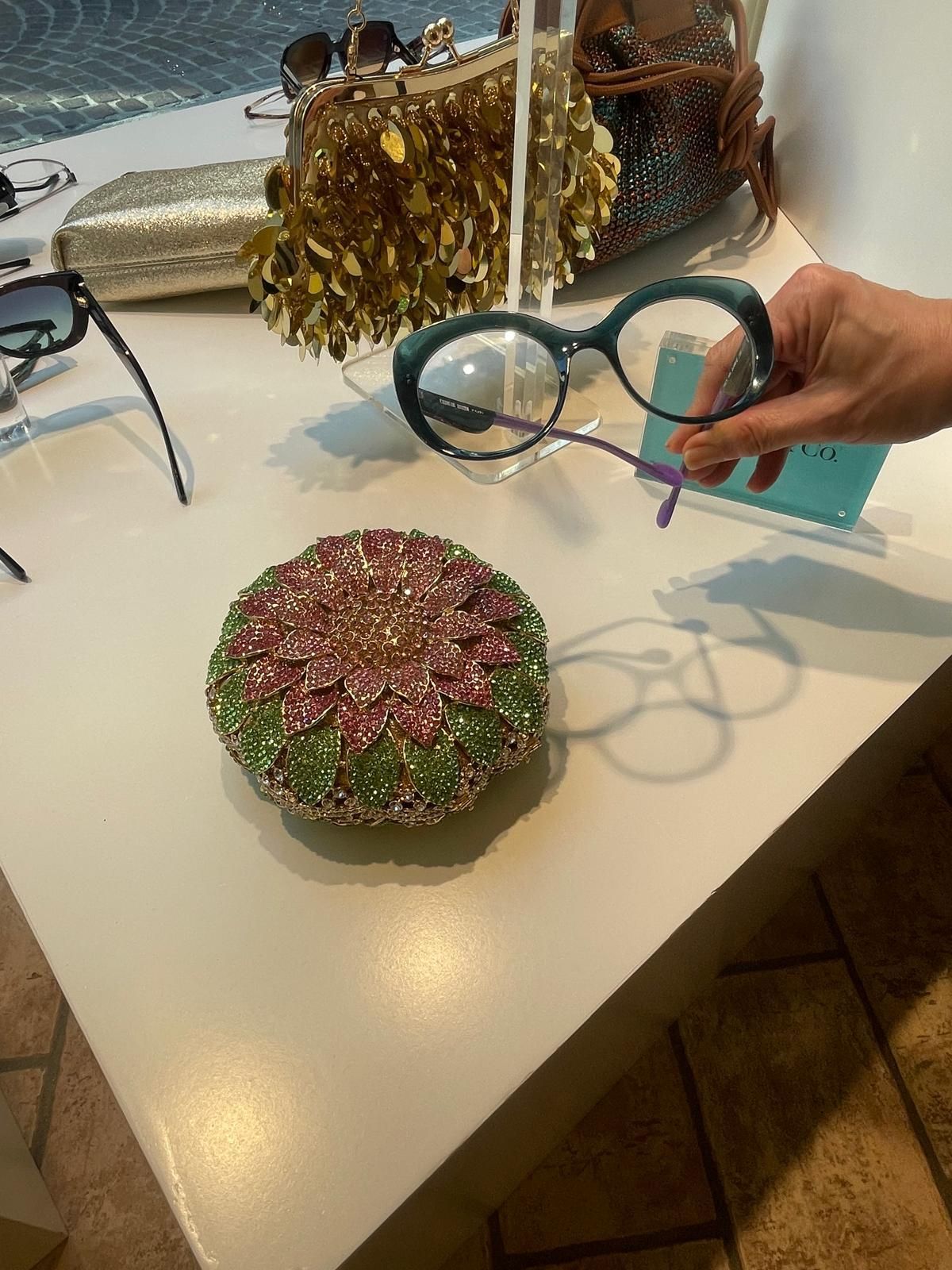 Una mano che regge bicchieri rotondi color verde acqua vicino ad accessori decorativi con perline su un tavolo bianco.