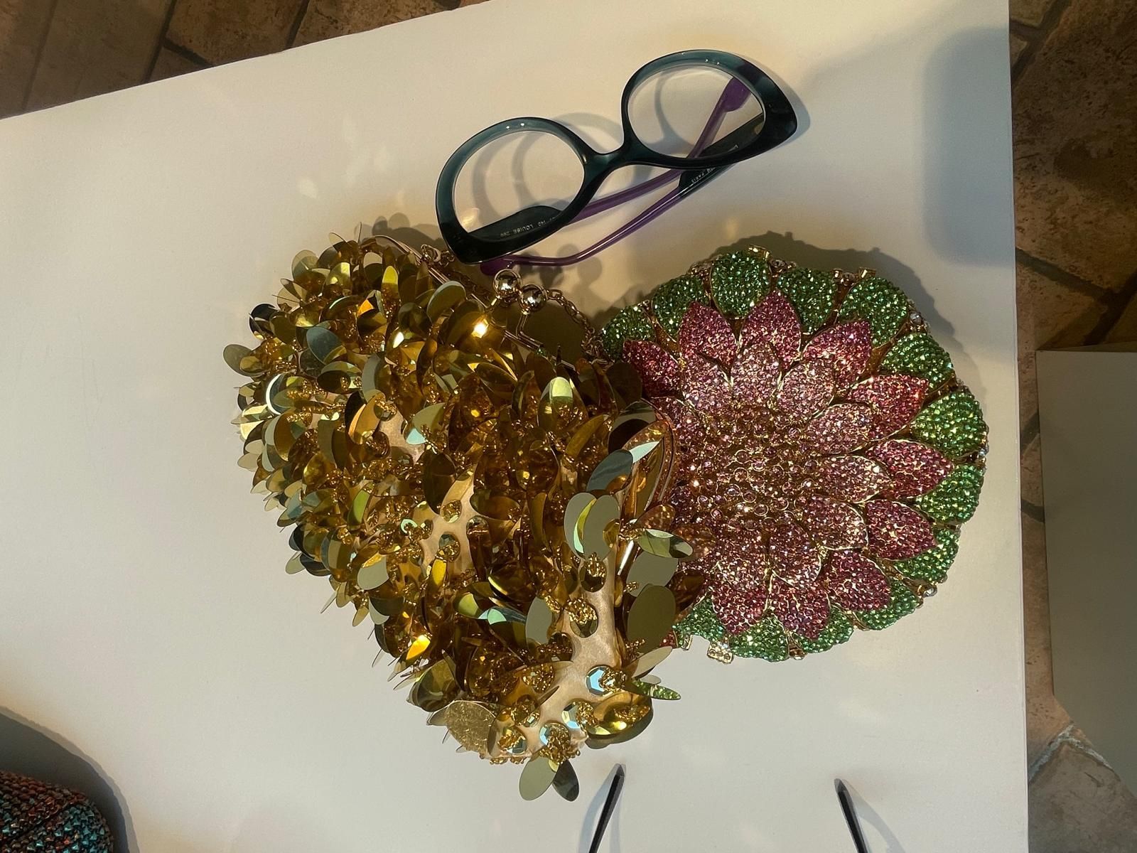 Due pompon decorativi scintillanti, uno dorato e uno rosa-verde, con manici in nastro blu su una superficie bianca.