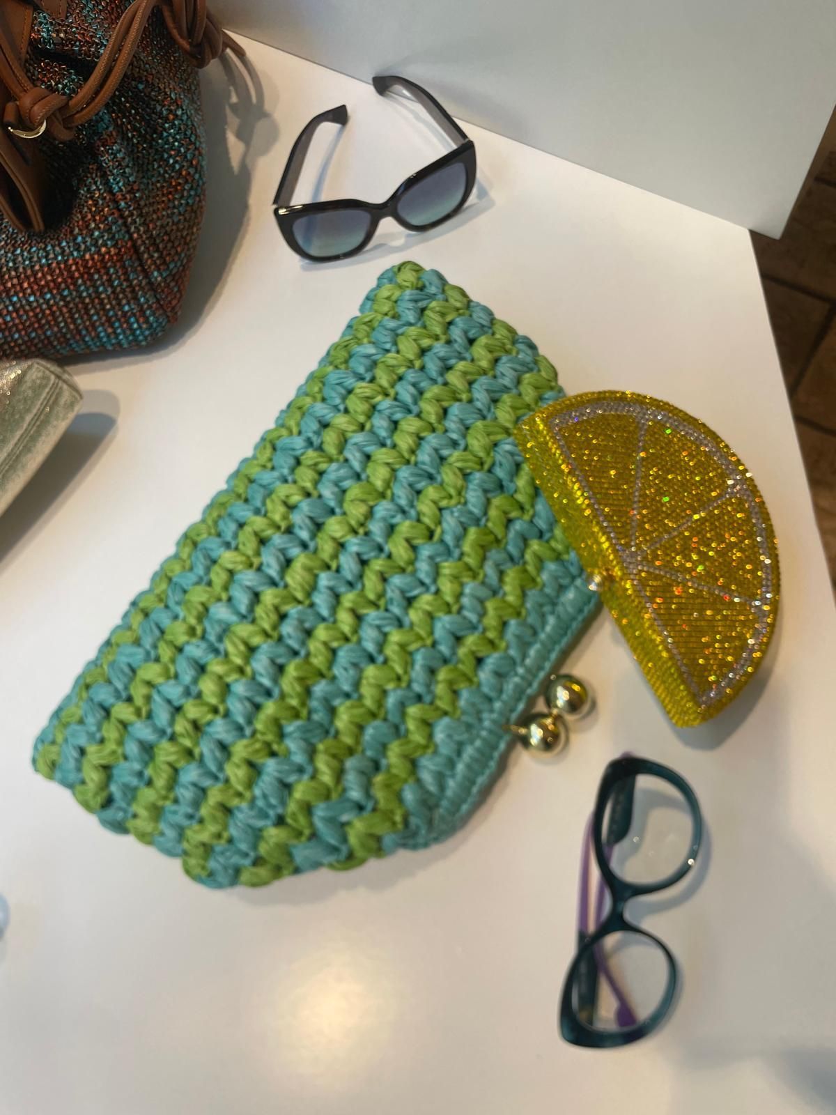 Due colorate pochette intrecciate su un tavolo bianco, con occhiali da sole e una borsa intrecciata nelle vicinanze.