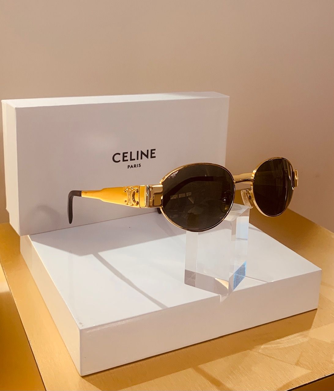 Occhiali da sole Celine con lenti rotonde scure e montatura dorata, esposti su una scatola bianca.
