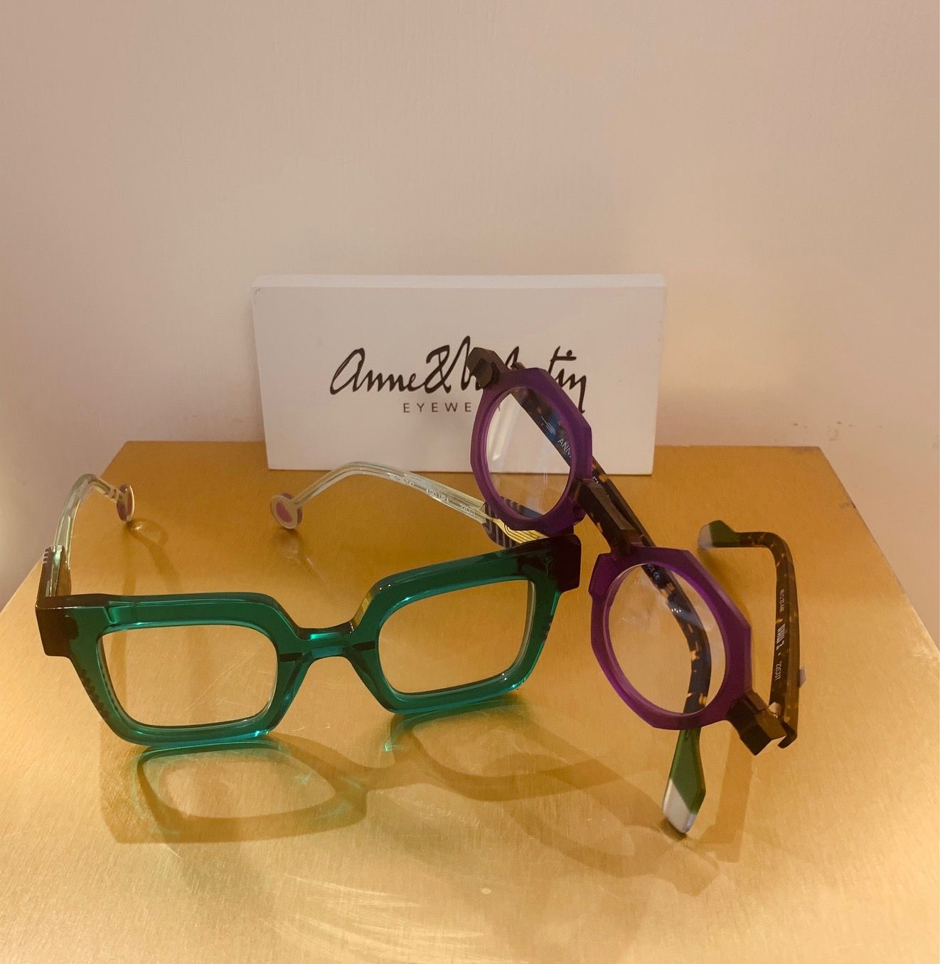 Due paia di occhiali, uno verde e uno viola, su una superficie dorata con un piccolo cartoncino dietro di essi