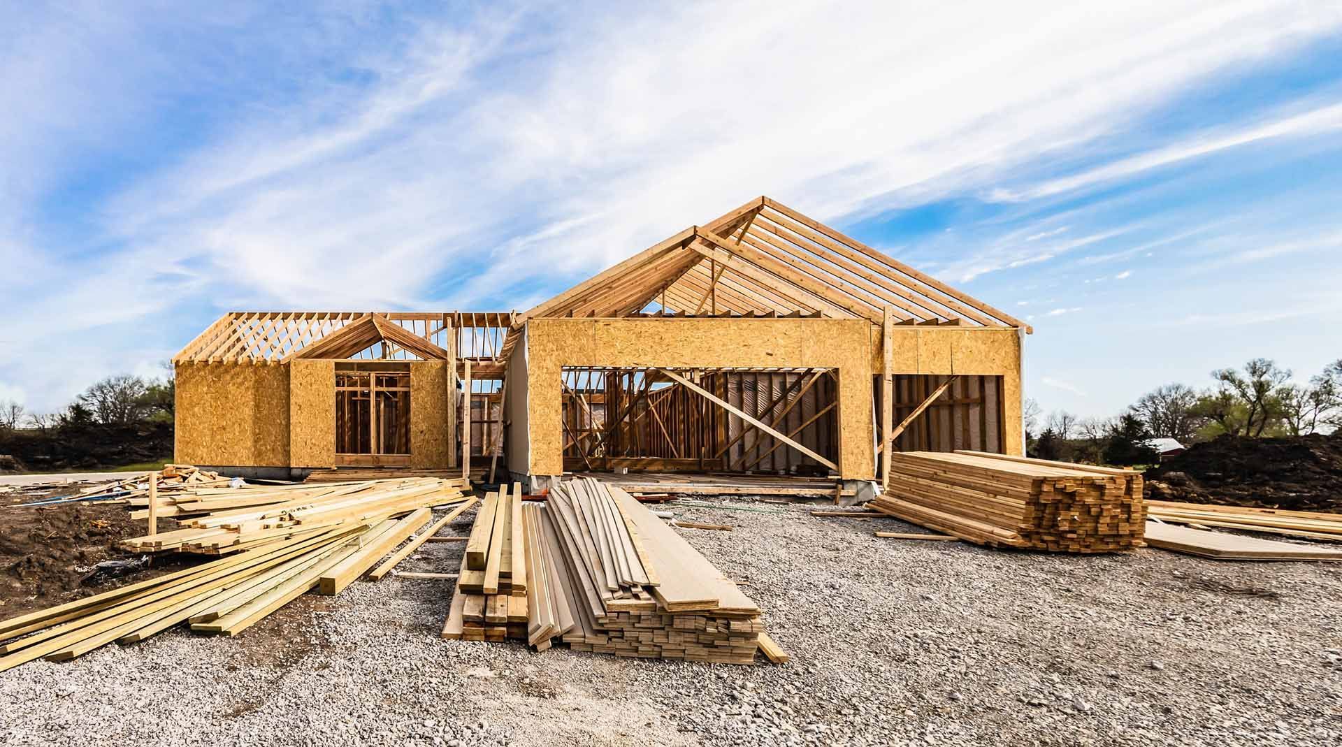 A wooden house is being built on a gravel lot