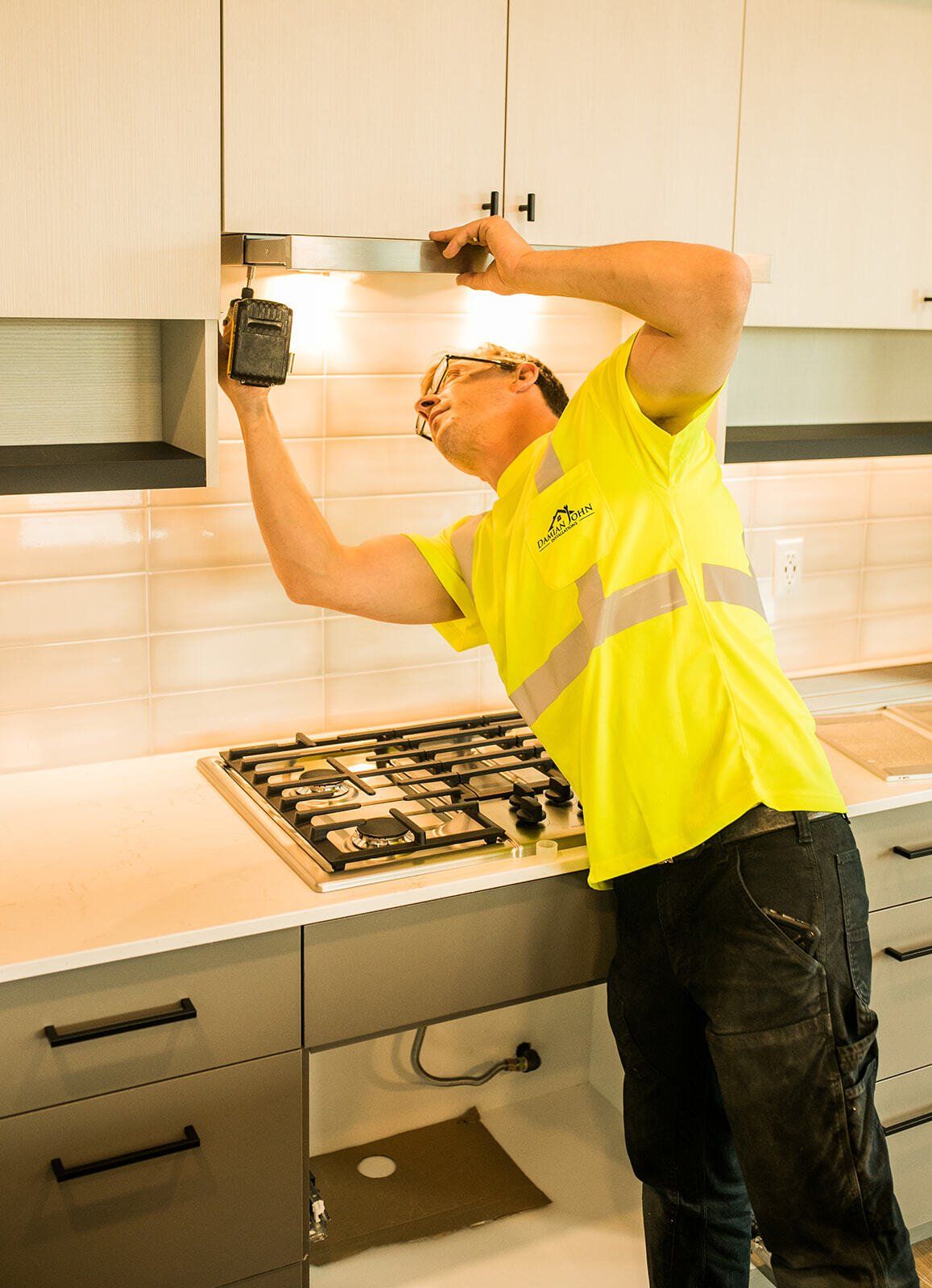 A man in a yellow shirt is working on a stove in a kitchen.